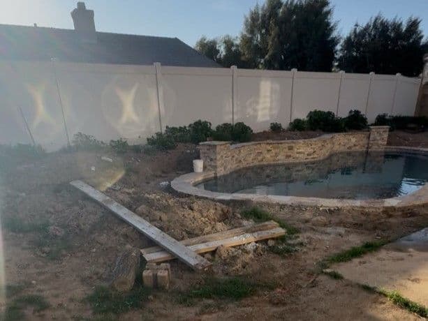 Under-construction backyard pool area with stone wall and dirt landscaping.